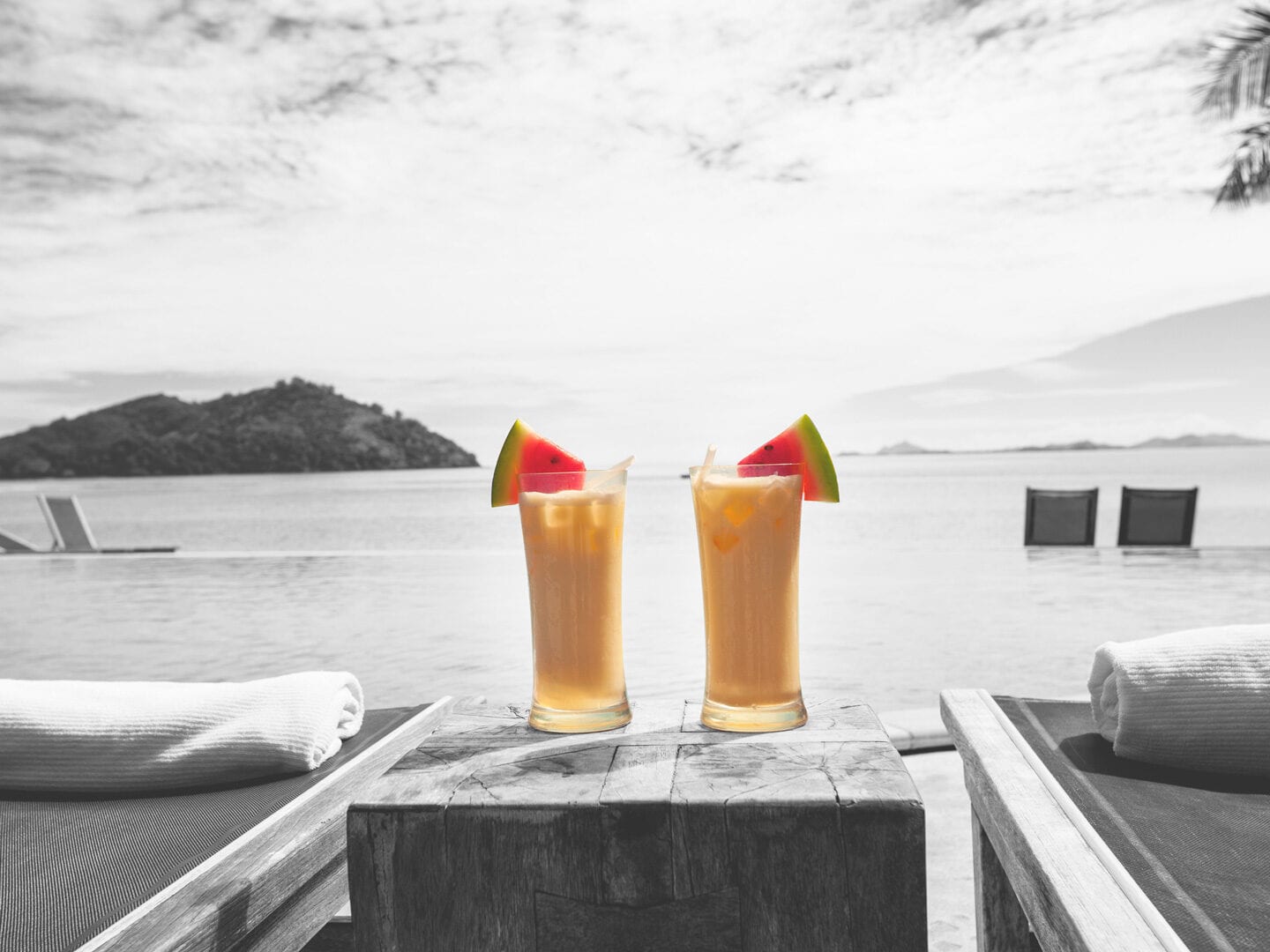 Zwei Cocktails stehen neben Sonnenliegen am Meer