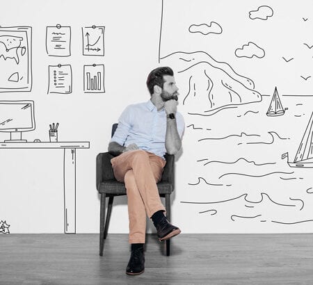 Ein Mann sitzt vor einem gemalten Hintergrund, uf dem ein Strand und ein Büro zu sehen sind.