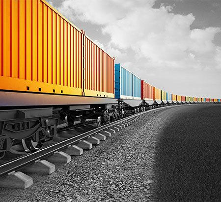 Ein Zug mit Containern mit Rohstoffen. Die Container sind bunt, der Himmel, der Boden und die Schienen sind schwarz und weiß.