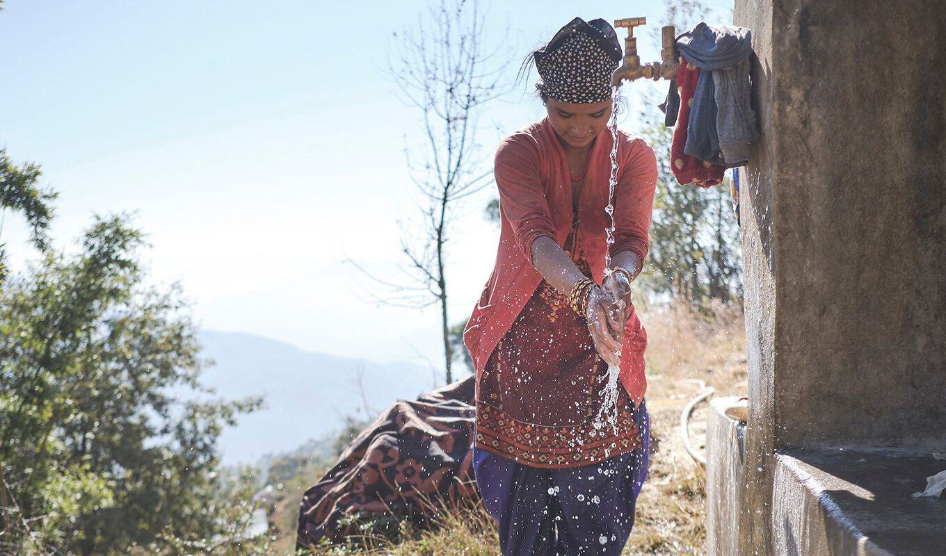 eine Frau in Nepal wäscht Hände und Kleidung an einem öffentlichen Wasserhahn