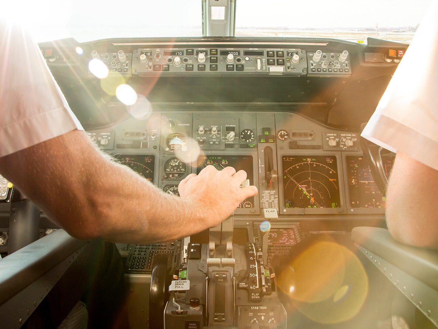 Foto aus dem Cockpit eines Flugzeugs, vom Piloten ist nur de rechte Hand zu sehen. Zum Start der Maschine wird der Starthebel nach vorn gedrückt, von von scheint Sonne ins Cockpit.