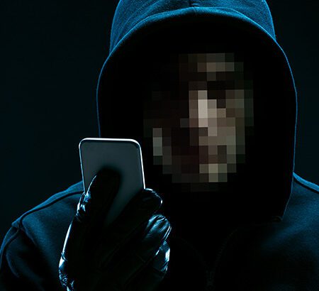 ein Mann mit verpixeltem Gesicht und schwarzem Kapuzen-Pullover schaut auf ein Smartphone
