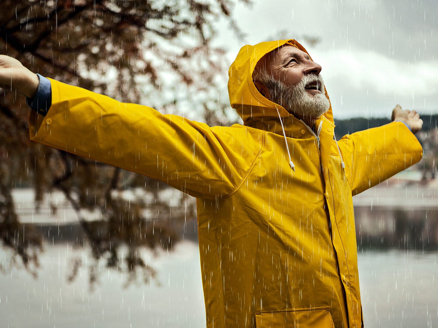 ein alter Mann steht im gelben Regenmantel mit ausgebreiteten Armen im strömenden Regen