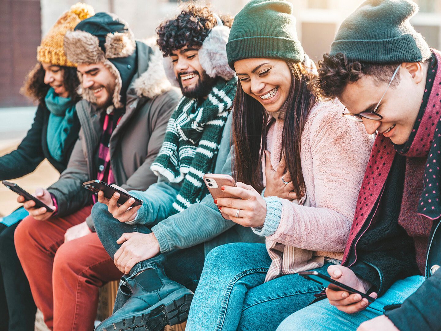 junge Frauen und Männer sitzen nebeneinander und schauen gut gelaunt auf ihre Smartphones