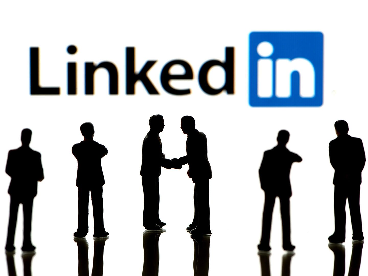 Symbolbild; Menschen stehen unter einem LinkedIn-Logo und netzwerken im realen Leben