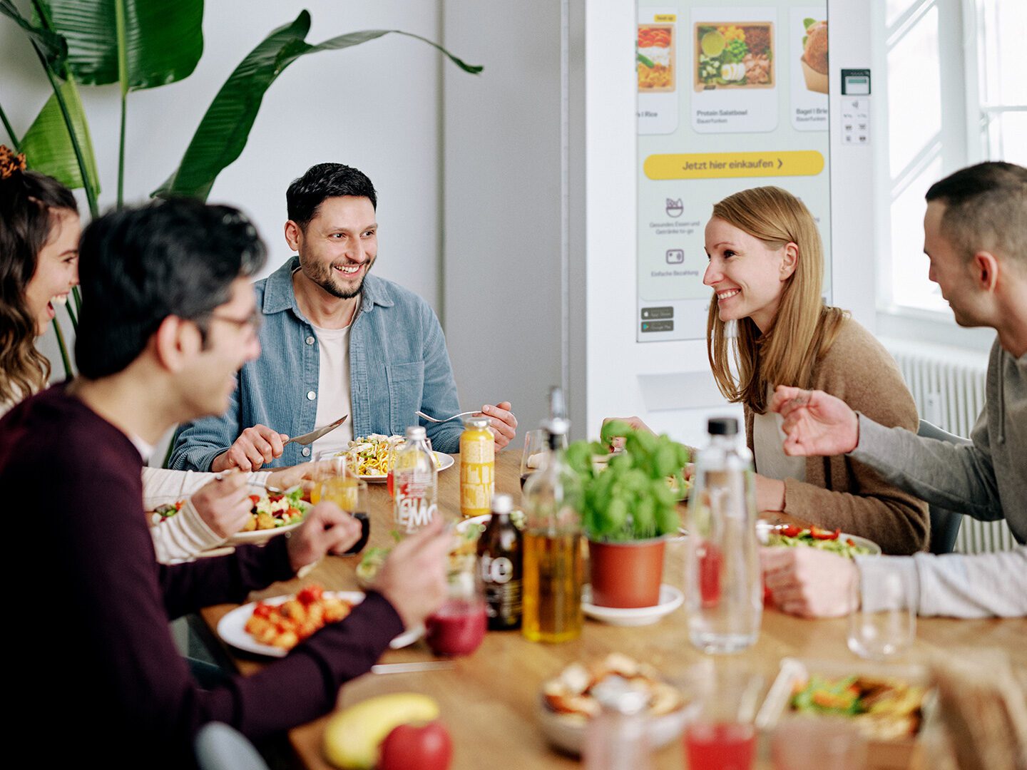 Mitarbeitende sitzen in der Pause zusammen und essen; im Hintergrund steht ein Essensautomat von Foodji