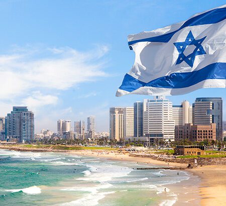 Israelische Flagge weht im Wind vor der Skyline und dem Strand von Tel Aviv und symbolisiert so Israels Wirtschaft