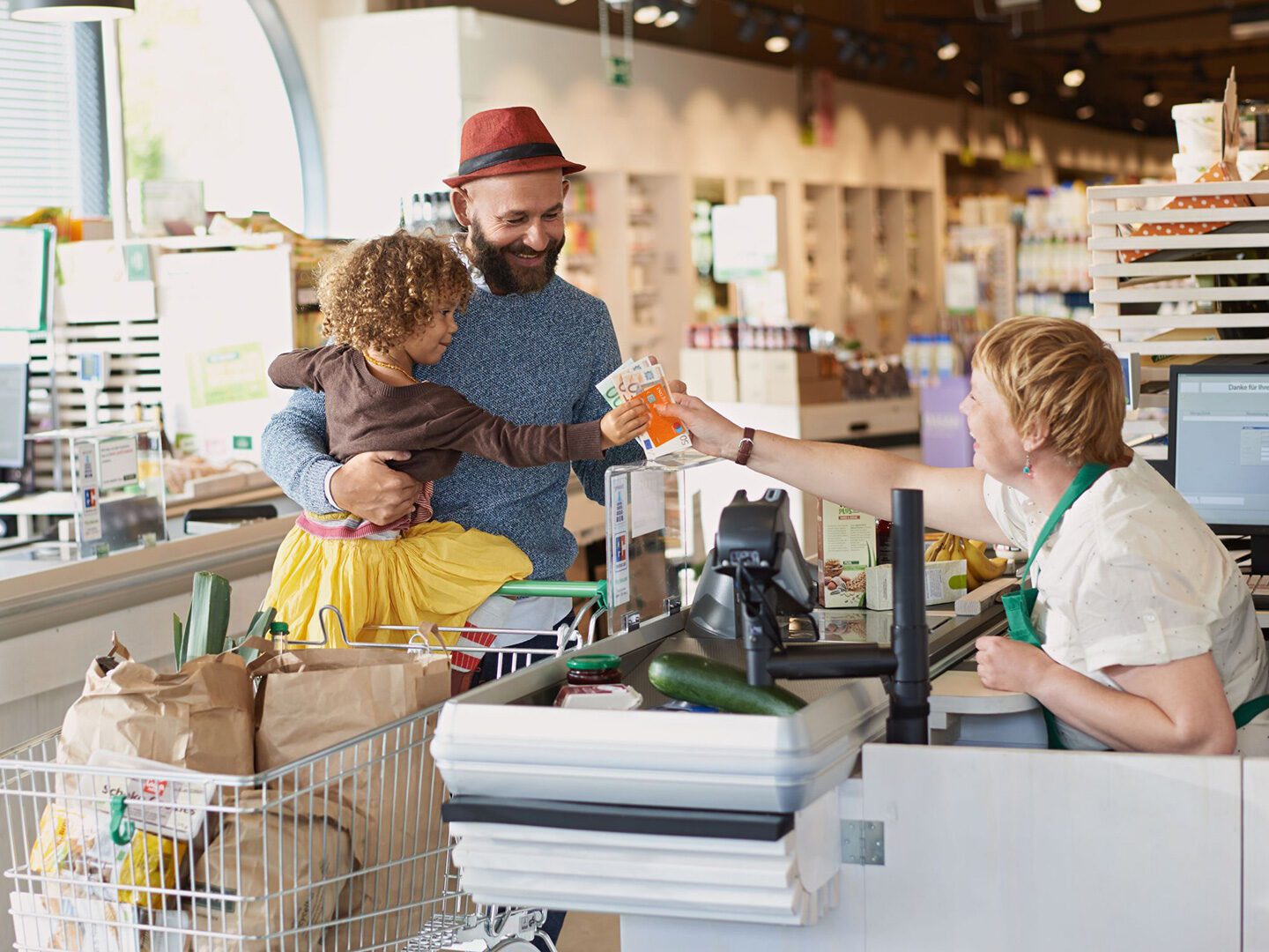 Ein Vater mit seinem Kind an der Supermarktkasse erhält Rückgeld, als Symbol für die Zinswende