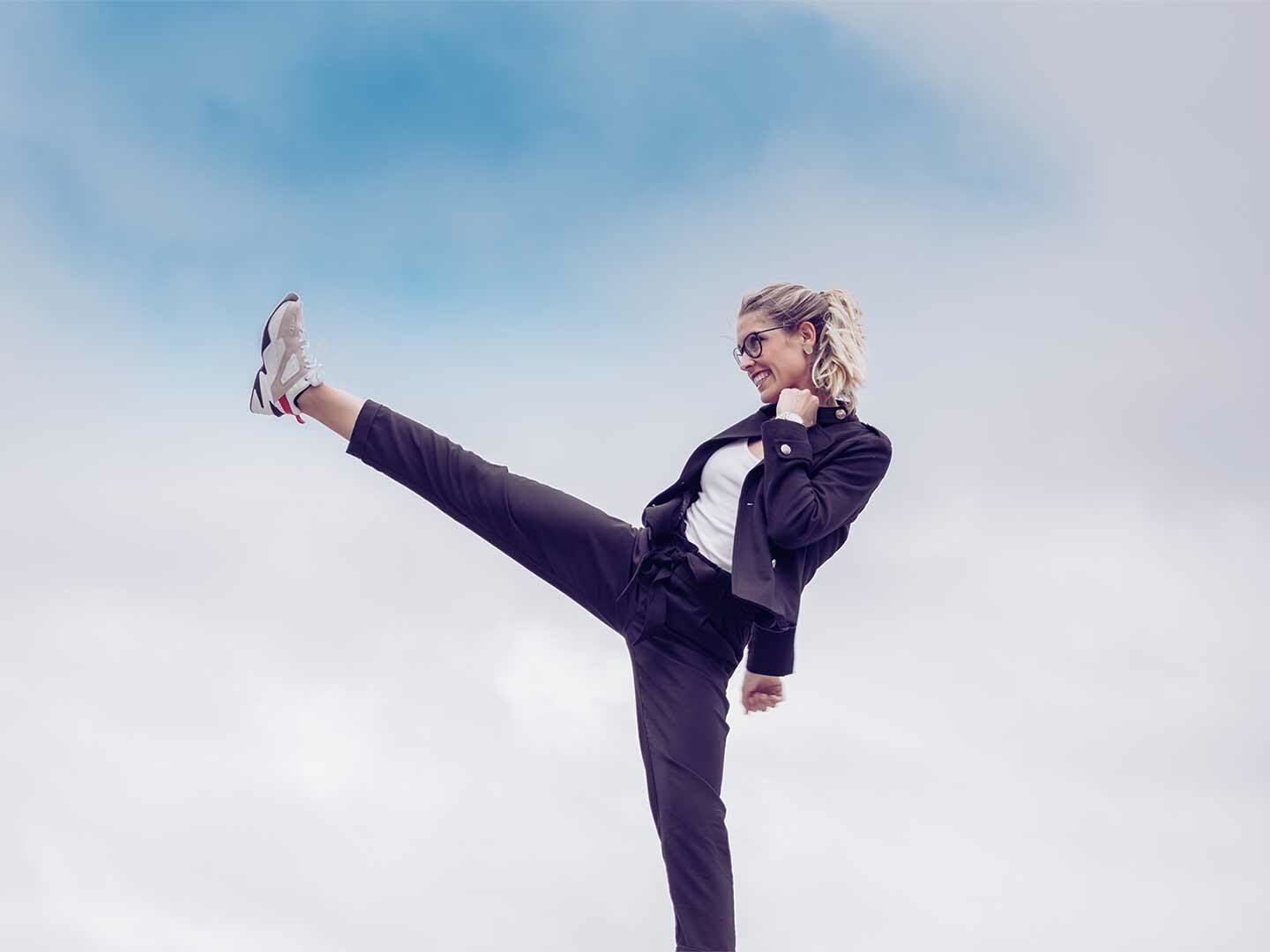 Eine Frau in Businesskleidung, die in die Luft tritt, um weibliche Stärke und den Weltfrauentag zu symbolisieren