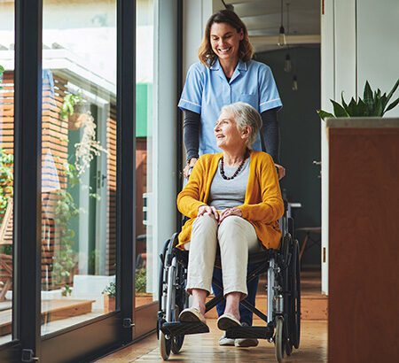 Pflegeversicherung: Symbolbild eine Pflegerin schiebt eine ältere Frau im Rollstuhl.